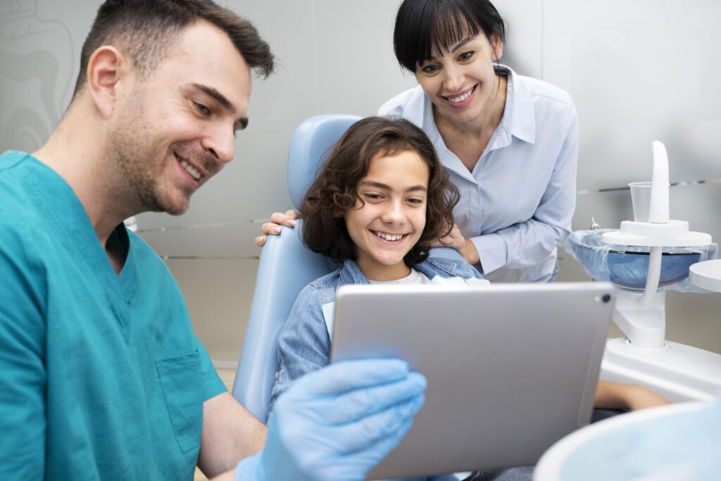 Equipo dental mostrando resultados a una niña con portátil, reflejando confianza y comunicación en clínicas dentales infantiles