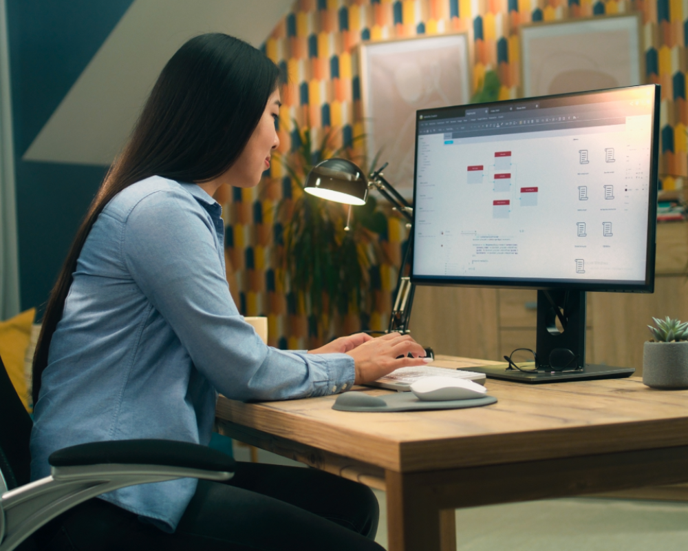 Mujer trabajando en su ordenador de escritorio desarrollando sitios web en un entorno productivo y organizado
