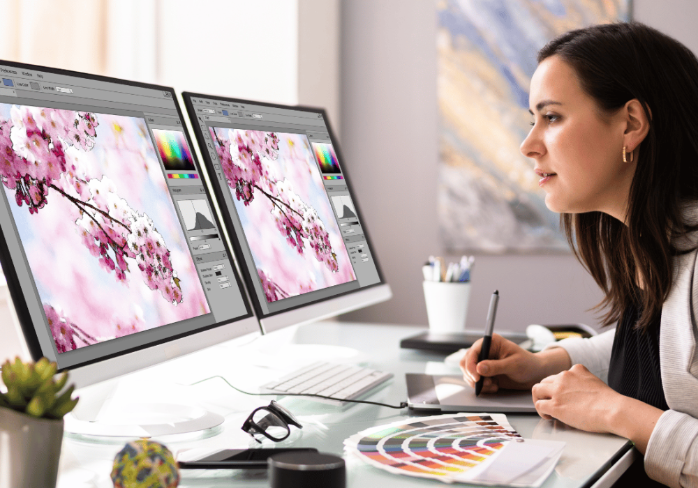 Mujer diseñando con doble monitor, reflejando un entorno creativo para el desarrollo de proyectos web y branding visual