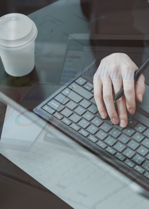 Manos escribiendo en teclado con café y gafas sobre la mesa, reflejando una jornada laboral en diseño web y posicionamiento