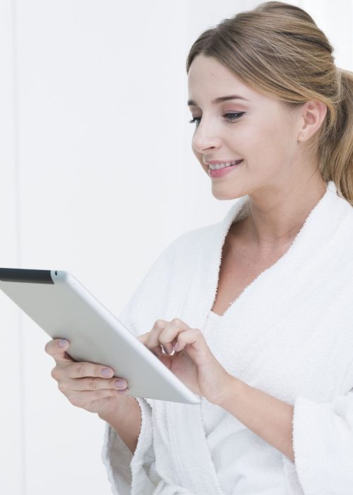 Mujer con bata blanca usando una tablet en clínica estética, representando una experiencia digital moderna y cómoda para el paciente